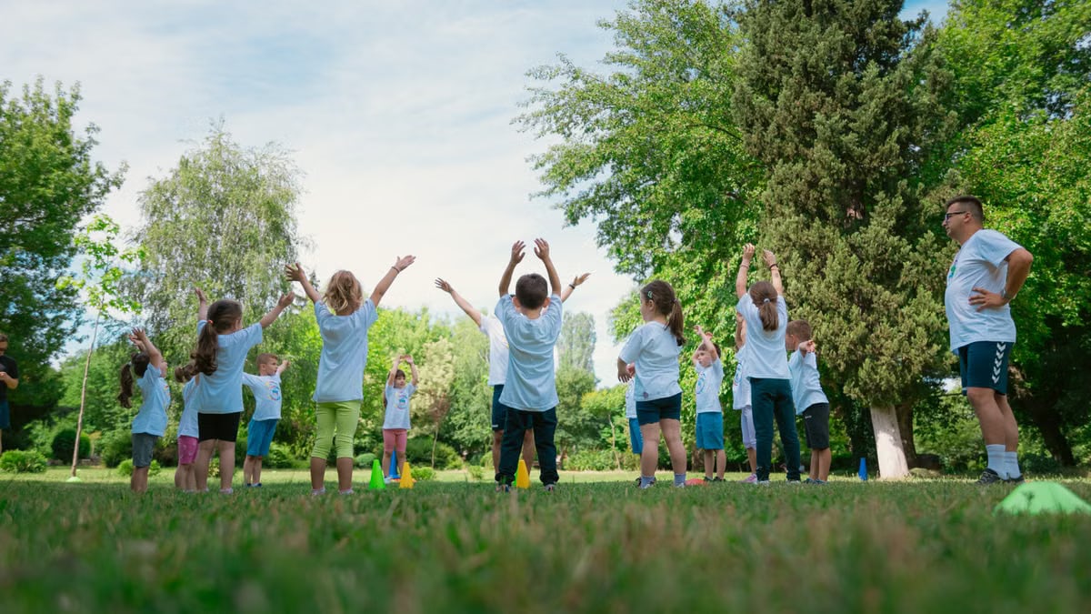 Group of children with instructor doing exercises in a sunny park setting, promoting outdoor activity.